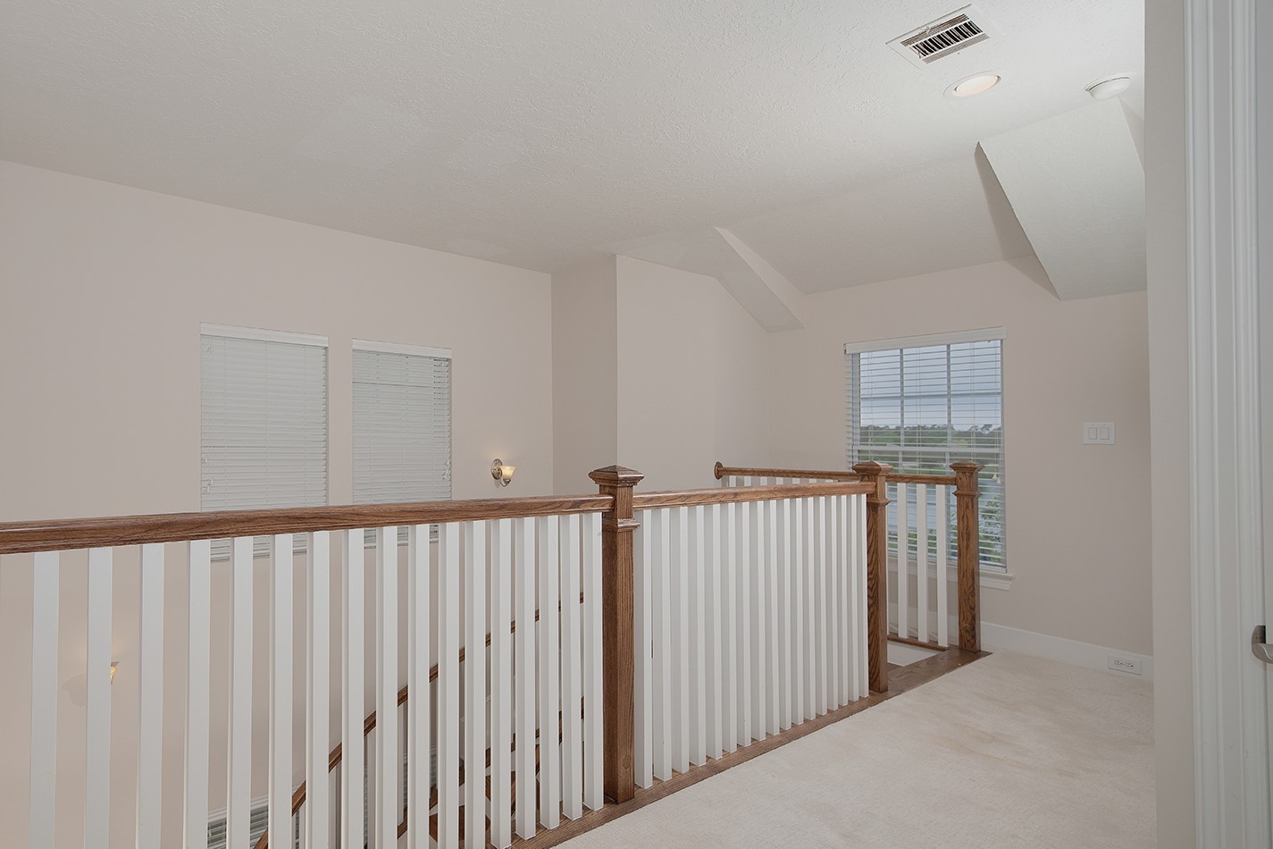 190 West Breezy Way Spring, TX 77380 - Photo 22 of 33 This photo shows a bright, open upstairs landing area with carpeted flooring, wooden banisters with white spindles, and multiple windows for natural light.
