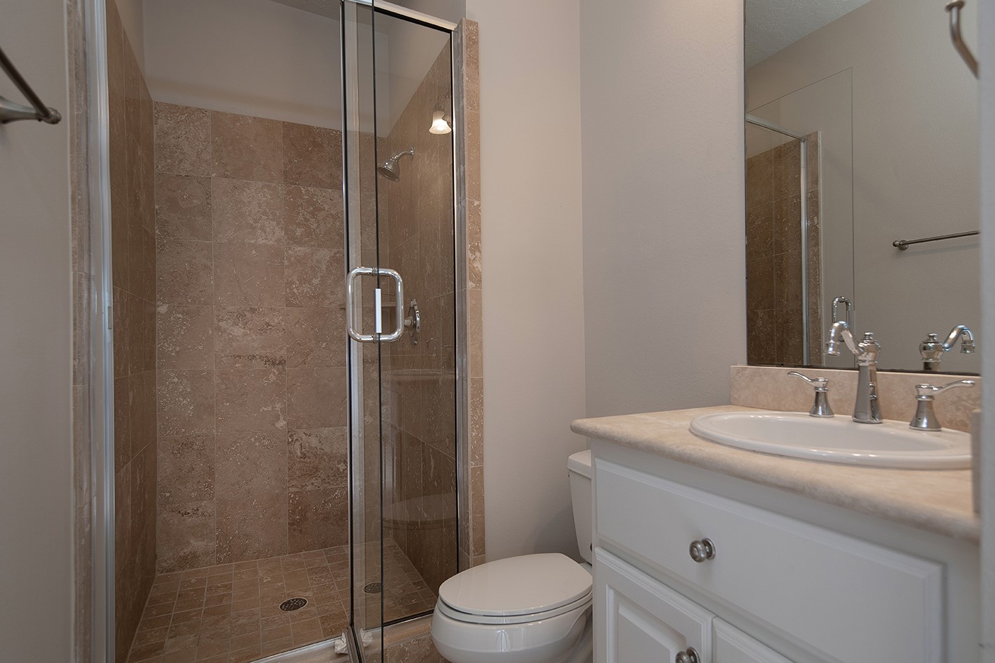190 West Breezy Way Spring, TX 77380 - Photo 29 of 33 This bathroom features a modern glass-enclosed shower with beige tile, a sleek white vanity with a polished countertop, and a built-in sink.