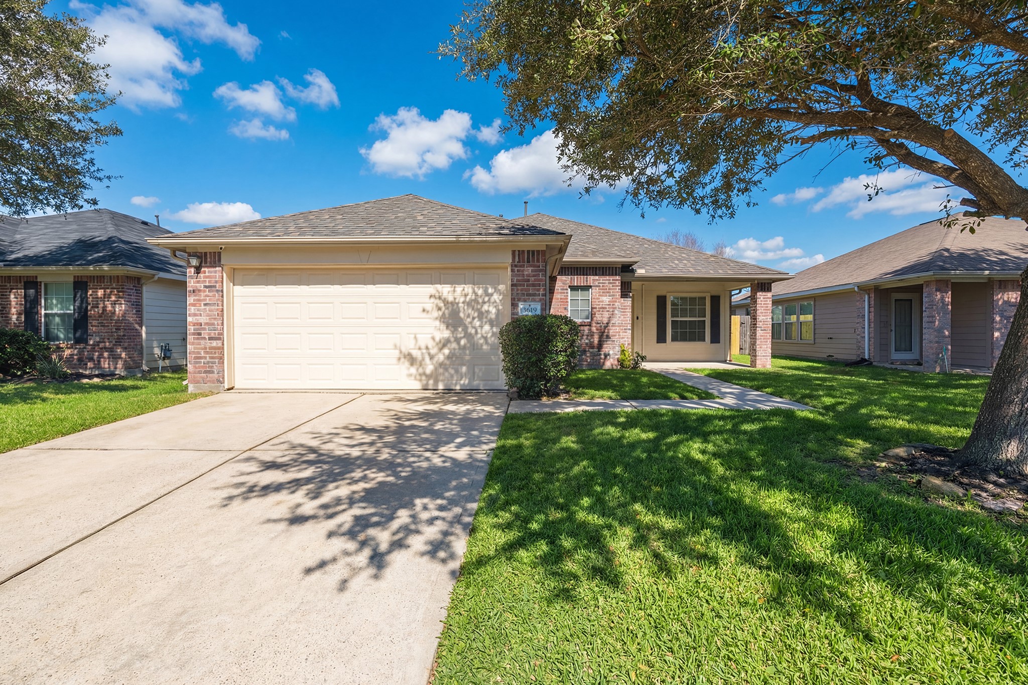 Charming single-story brick home with a two-car garage, set in a well-maintained neighborhood. Features a spacious driveway, lush green lawn, and a welcoming front porch under a shade tree. Perfect for comfortable suburban living.