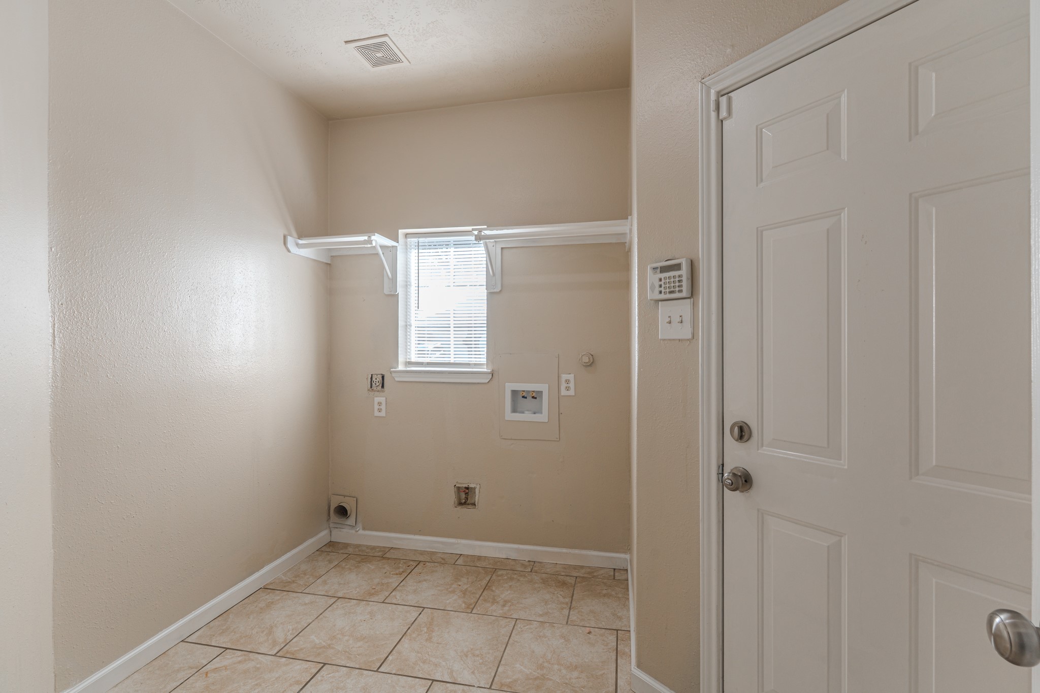 3619 Fiorella Way Humble, TX 77338 - Photo 14 of 16 This is a utility or laundry room with beige walls and tiled flooring. It features connections for a washer and dryer, a small window for natural light, and a door leading to another area.