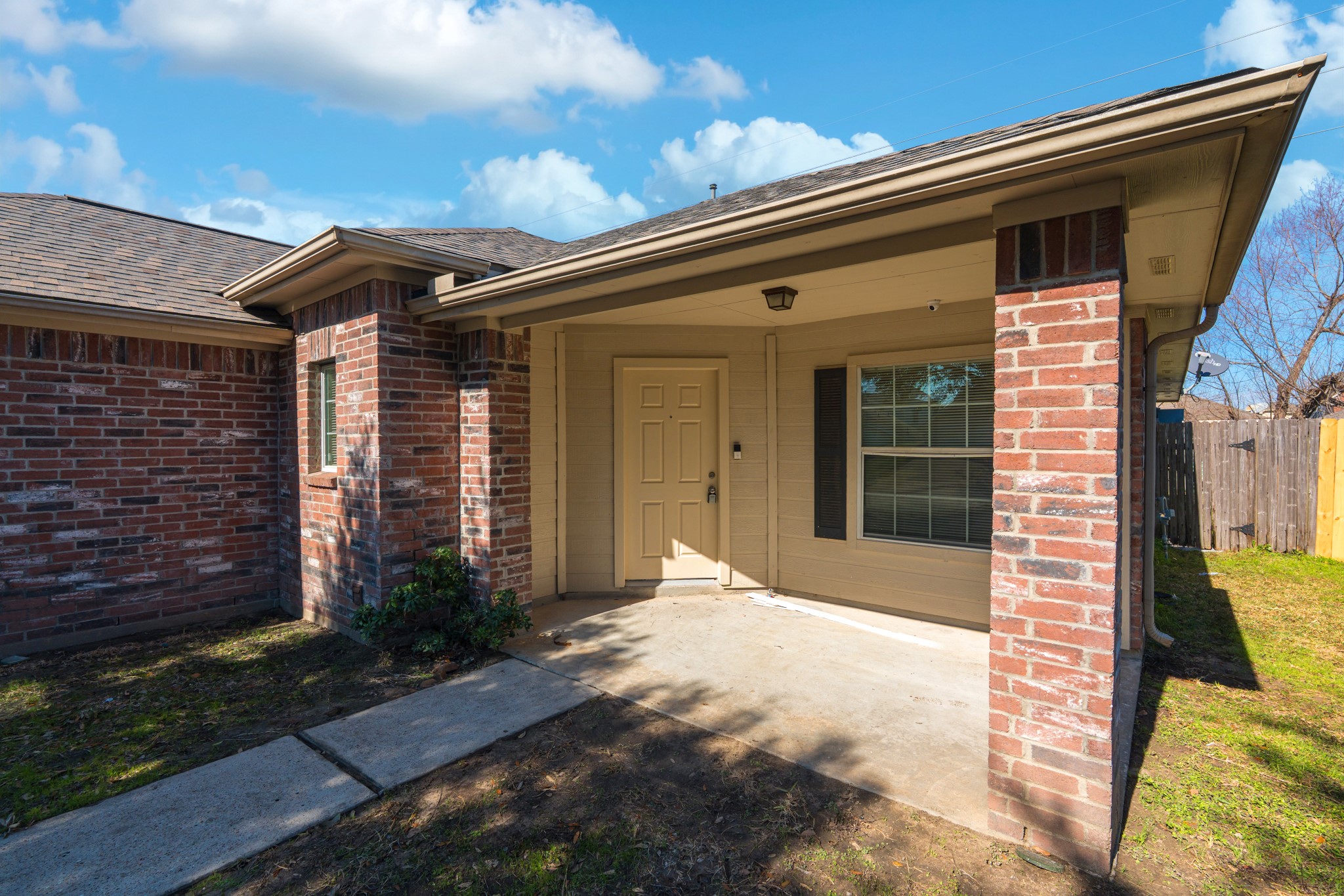 3619 Fiorella Way Humble, TX 77338 - Photo 2 of 16 A cozy brick home with a covered front porch, featuring a single door entry and a large window. The yard is partially shaded, surrounded by a wooden fence, and offers a welcoming entrance.
