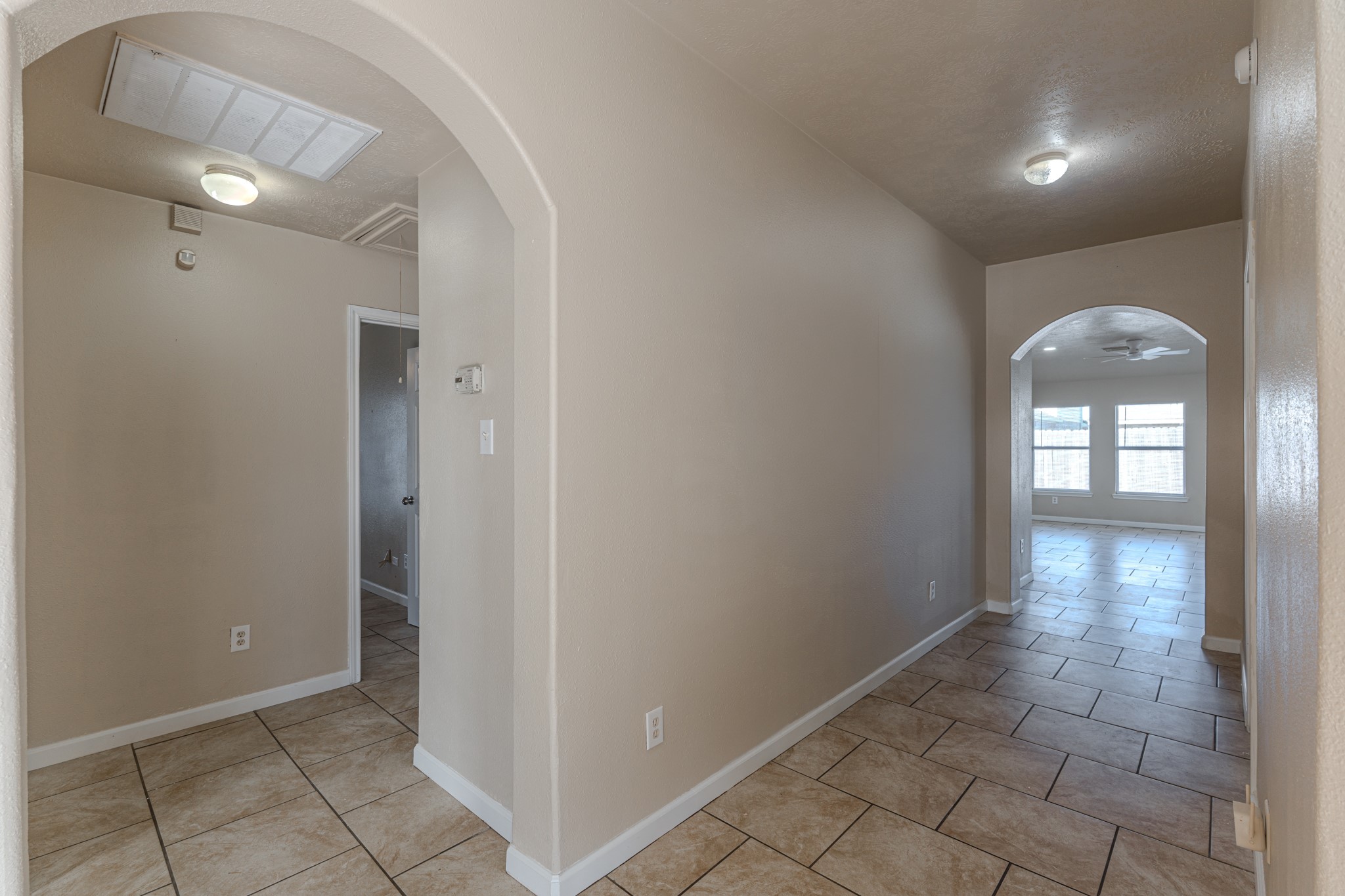 3619 Fiorella Way Humble, TX 77338 - Photo 3 of 16 This photo shows a clean, neutral-toned hallway with tiled flooring and arched doorways, leading into a bright room with large windows.