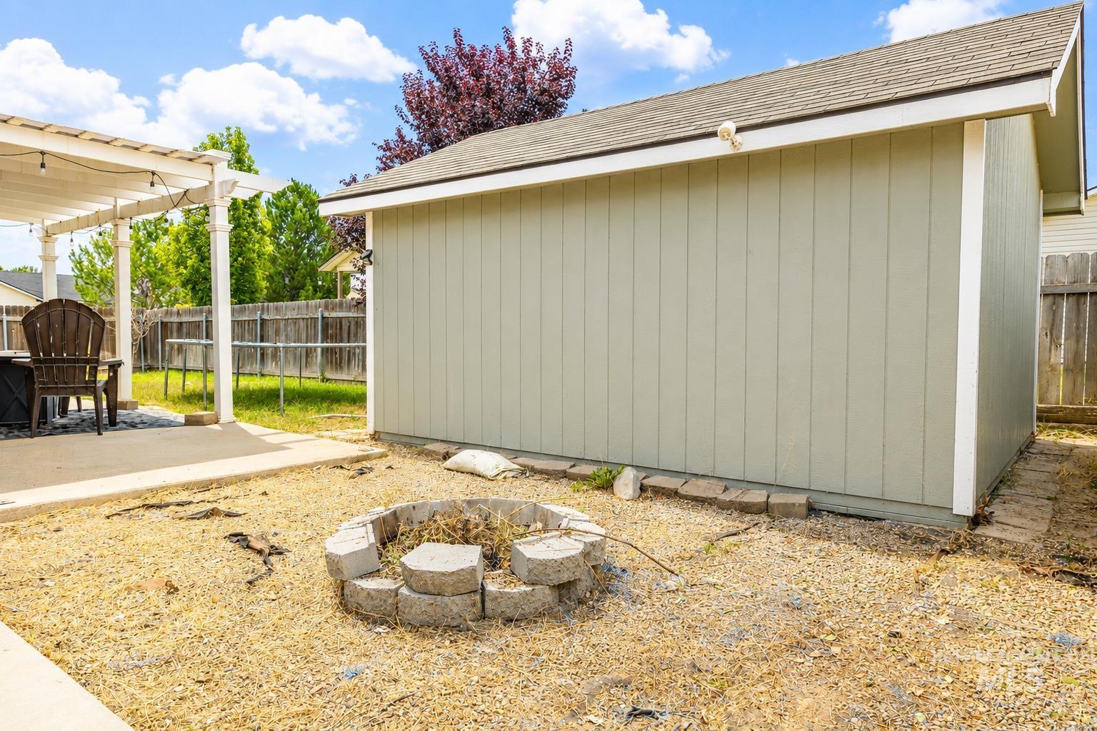 14409 Raleigh Court Caldwell, ID 83607 - Photo 14 of 15 Backyard featuring a concrete patio, white pergola, gravel hardscaping, and a built-in stone fire pit