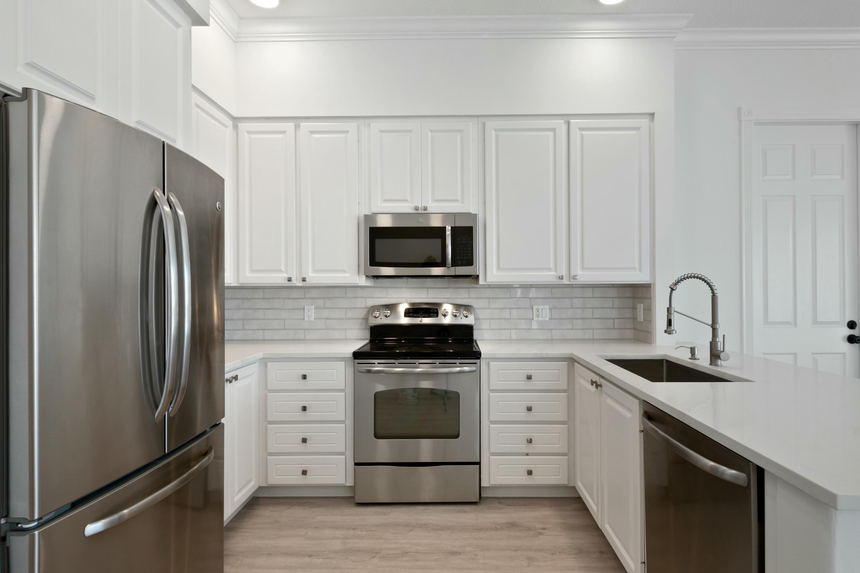 140 Barbados Drive Jupiter, FL 33458 - Photo 40 of 42 a kitchen with white cabinets and stainless steel appliances
