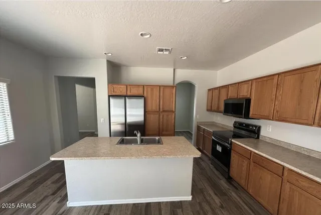 a kitchen with stainless steel appliances kitchen island granite countertop a refrigerator a sink a stove and a refrigerator with wooden floor