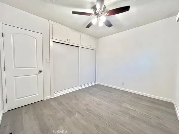an empty room with wooden floor closet fan and windows