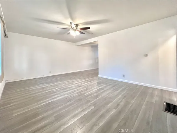 an empty room with wooden floor fan and windows