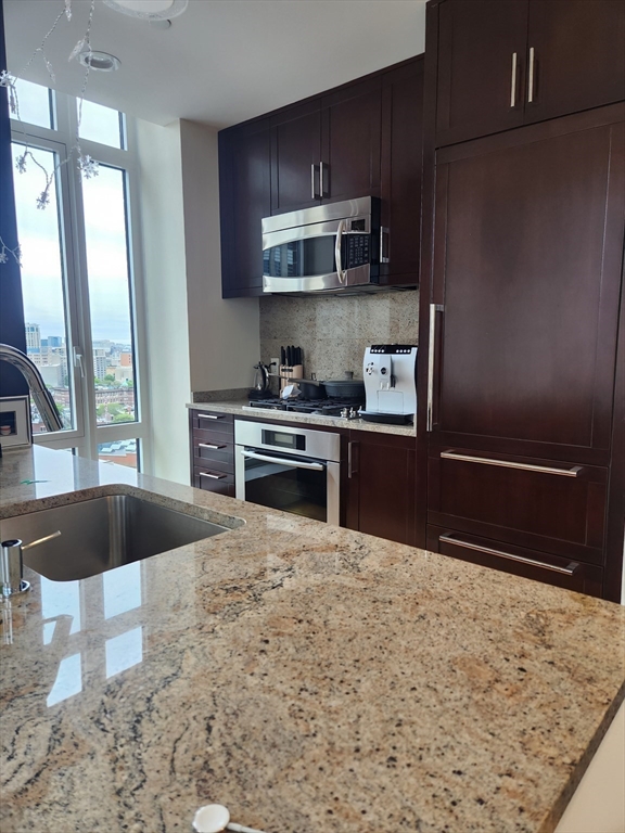 400 Stuart Street, Unit 18K Boston, MA 02116 - Photo 5 of 29 a kitchen with stainless steel appliances granite countertop a refrigerator a stove and a sink with wooden cabinets