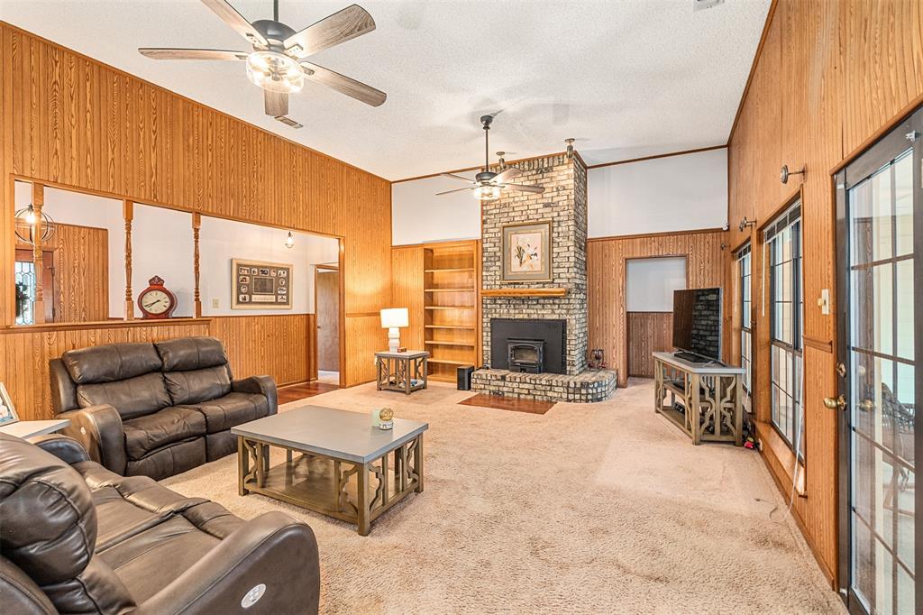 1199 Cedar Lane Kaufman, TX 75142 - Photo 9 of 40 Carpeted living area featuring wood walls, a textured ceiling, built in features, a fireplace, and lofted ceiling