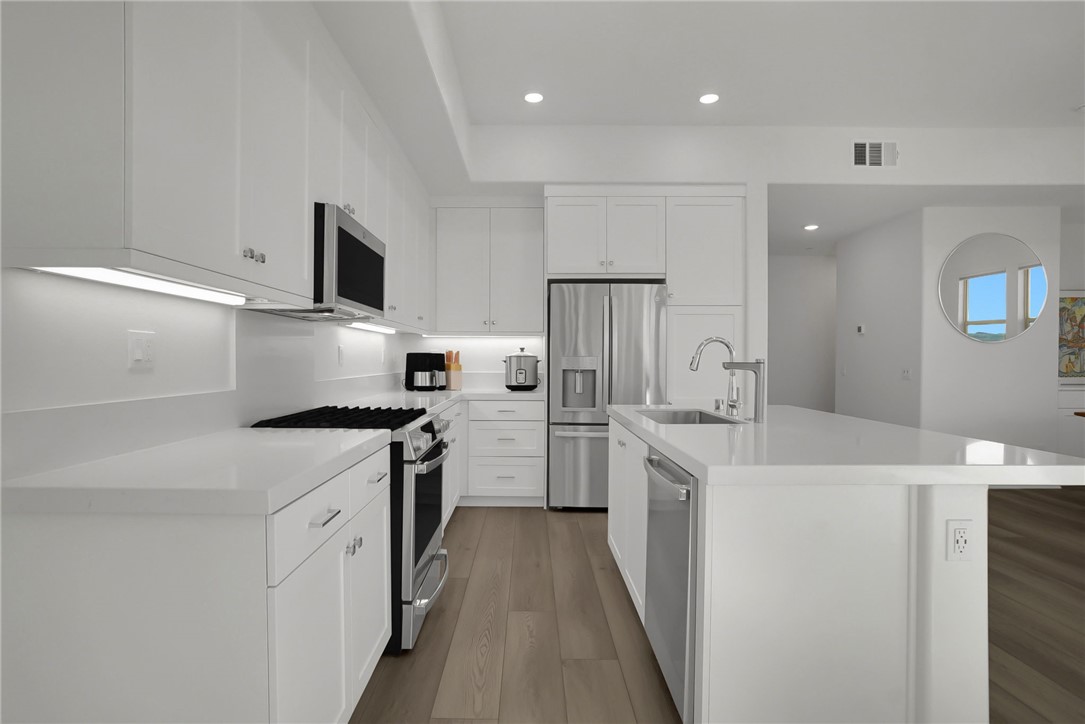 1958 Hollyleaf Terrace Montebello, CA 90640 - Photo 16 of 58 a kitchen with stainless steel appliances a sink dishwasher stove refrigerator and white cabinets with wooden floor