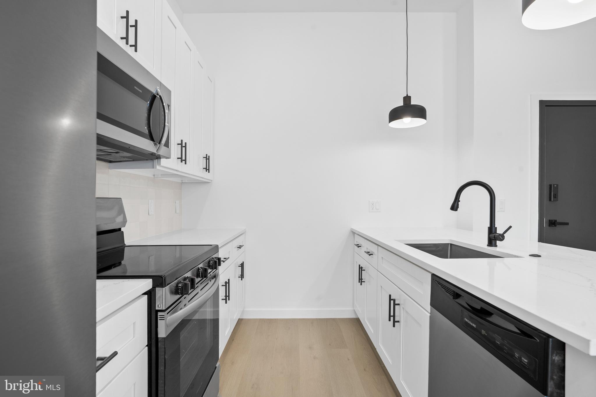3211 Cedar Street, Unit 401 Philadelphia, PA 19134 - Photo 5 of 18 a kitchen with stainless steel appliances a sink dishwasher a stove and a microwave with wooden floor