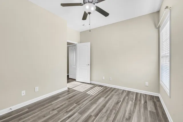 a view of an empty room with wooden floor and a ceiling fan