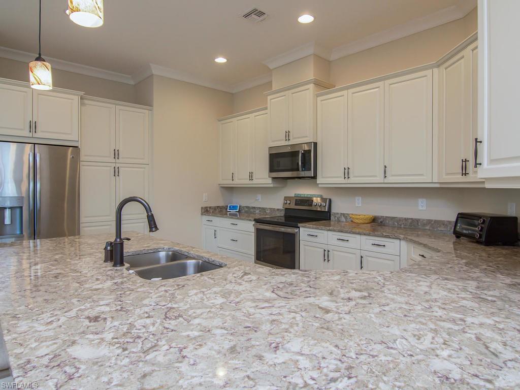 7002 Dominica Drive Naples, FL 34113 - Photo 11 of 33 a kitchen with kitchen island granite countertop a stove sink and cabinets