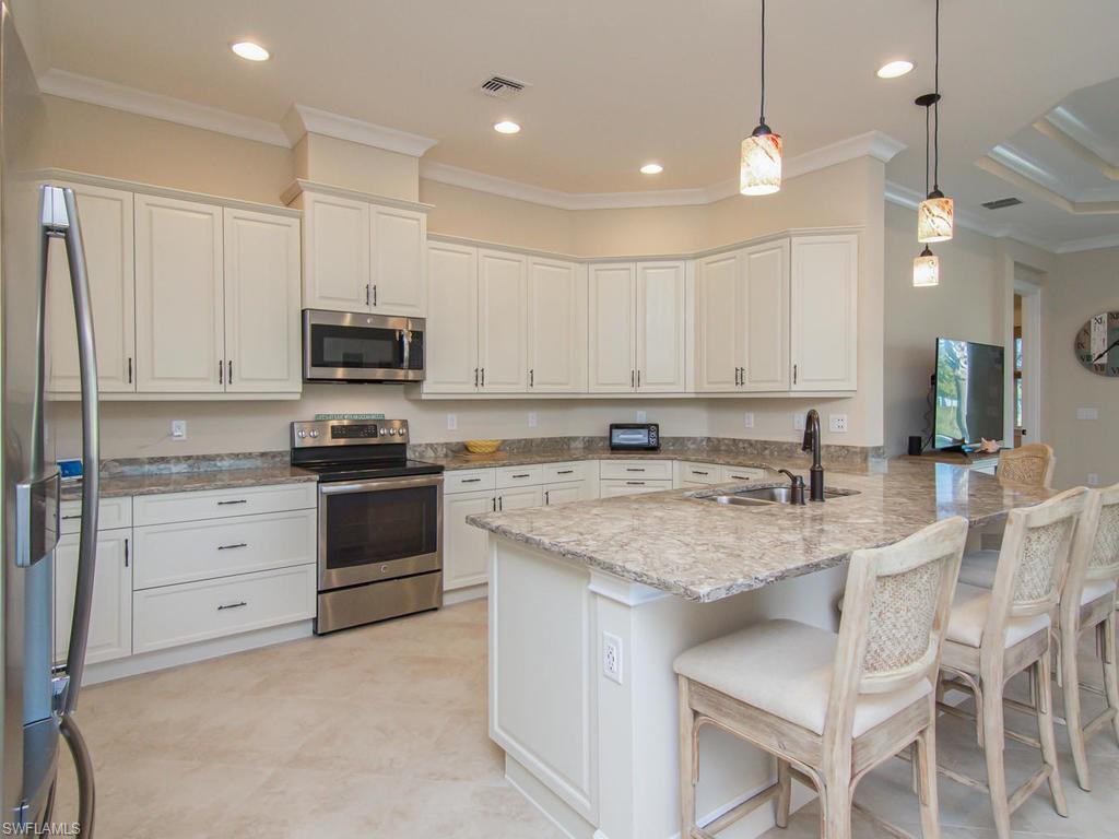 7002 Dominica Drive Naples, FL 34113 - Photo 12 of 33 a kitchen with kitchen island granite countertop white cabinets and stainless steel appliances