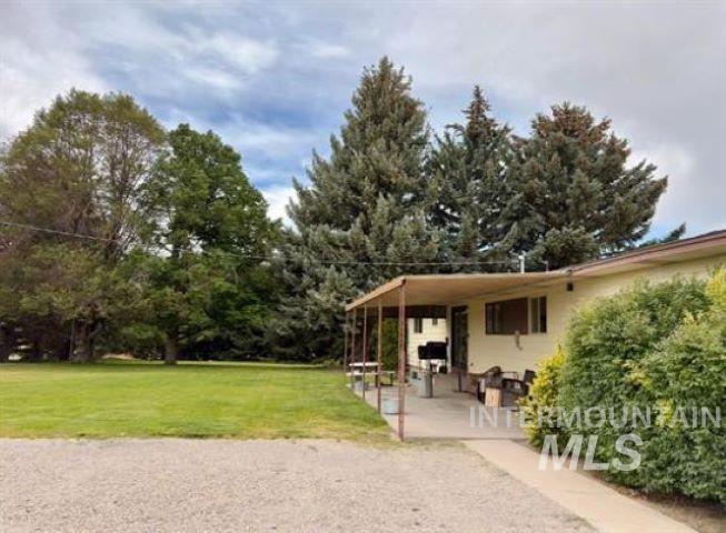 3197 Neeley Road American Falls, ID 83211 - Photo 36 of 45 Rear exterior featuring a covered patio, extensive gravel driveway, lush green lawn, mature trees, and established perimeter shrubbery