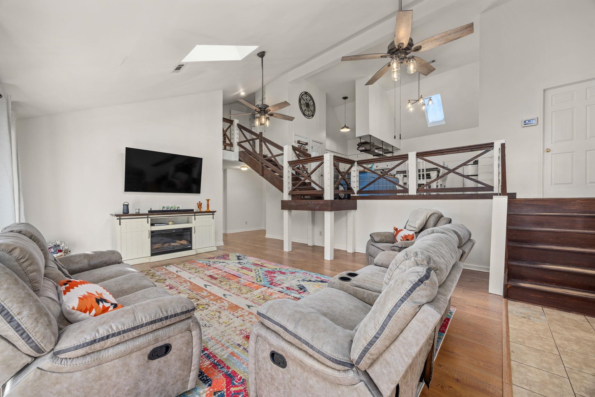 Living room featuring ceiling fan, wood-type flooring, a skylight, and high vaulted ceiling