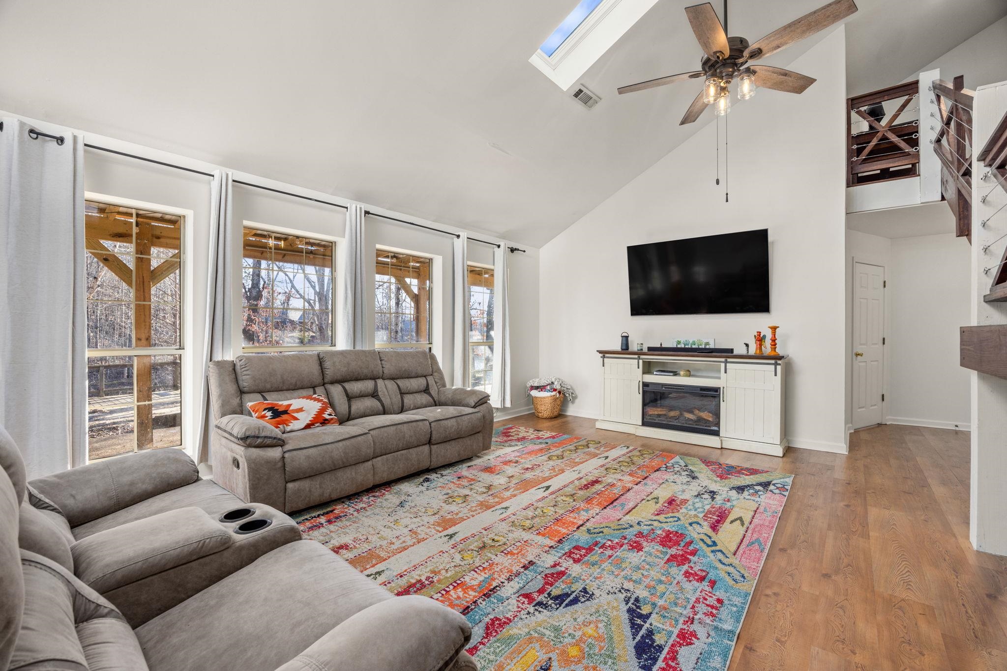 Living room with ceiling fan, high vaulted ceiling, a skylight, and light hardwood / wood-style floors