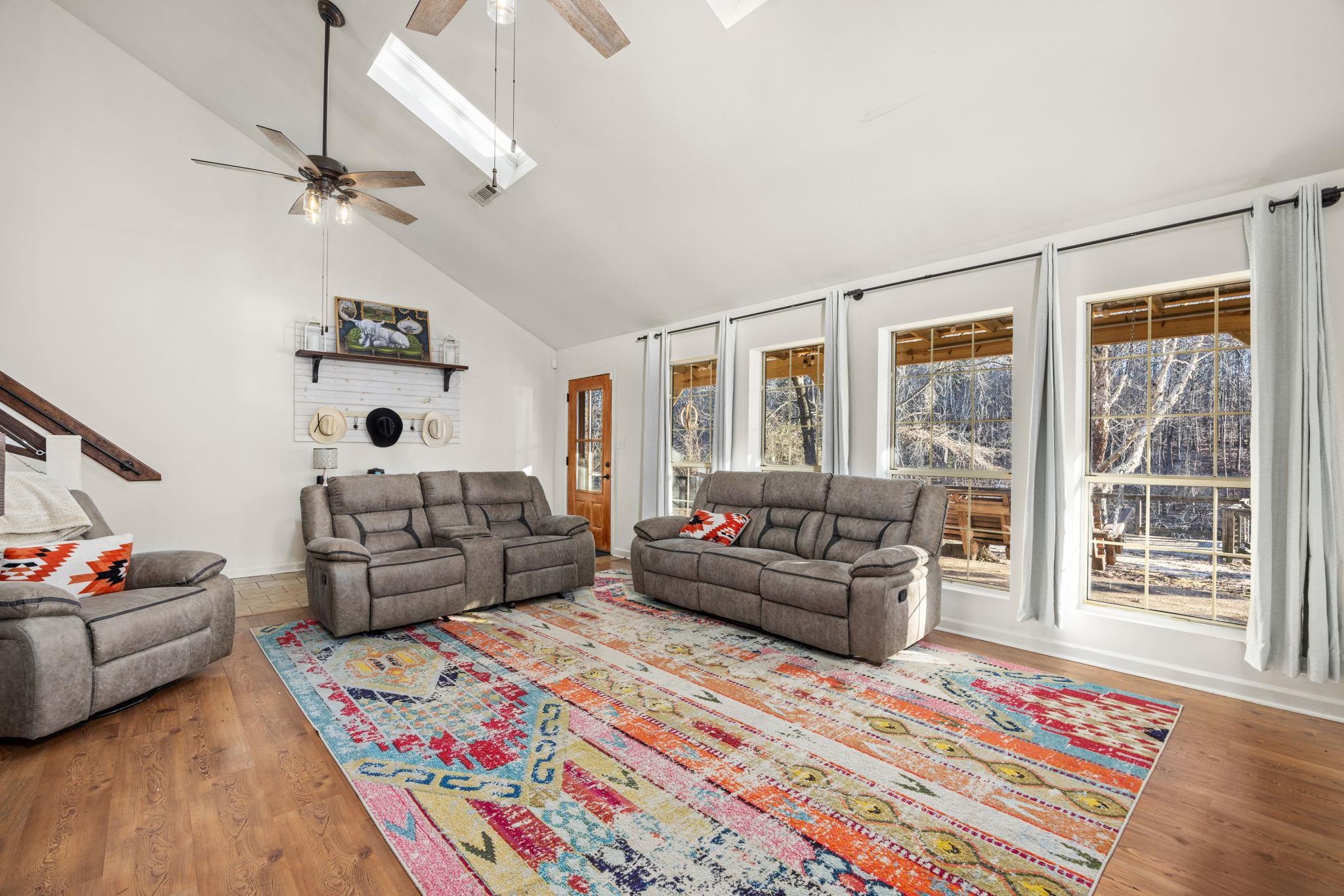 Living room with ceiling fan, high vaulted ceiling, light hardwood / wood-style floors, and a skylight