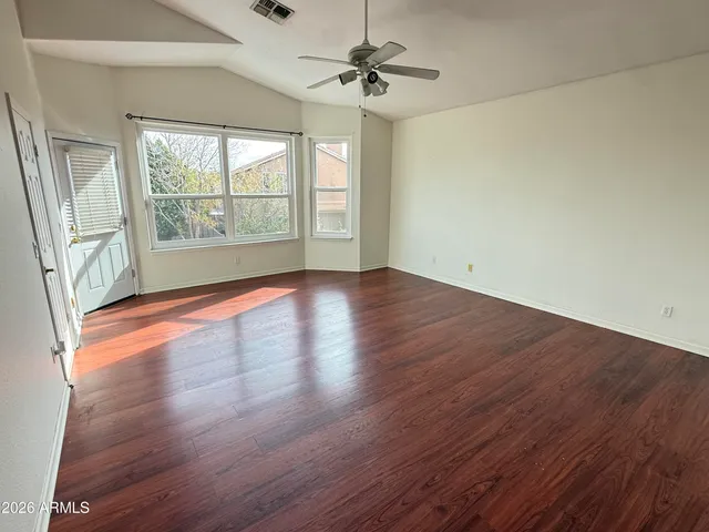 an empty room with wooden floor chandelier fan and windows