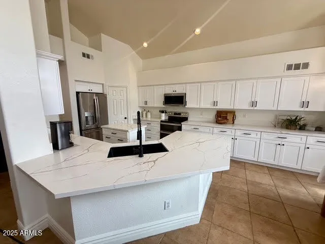 a kitchen with kitchen island granite countertop a sink a stove a refrigerator cabinets and chairs