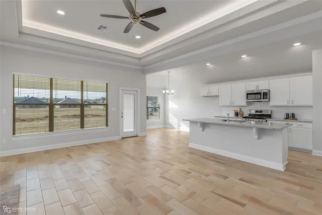 a large white kitchen with kitchen island a stove a sink dishwasher and white cabinets with wooden floor