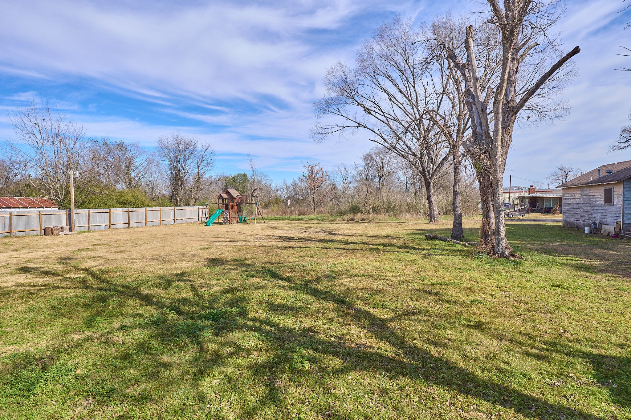 1807 Nuches Lane Bryan, TX 77803 - Photo 24 of 27 Spacious backyard with a wooden playset, bordered by a fence, and featuring mature trees. Ideal for families seeking outdoor space.