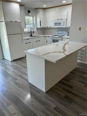 a kitchen with stainless steel appliances granite countertop a sink a stove a refrigerator and white cabinets with wooden floor