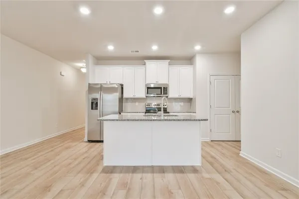 a kitchen with stainless steel appliances granite countertop a sink a stove a refrigerator and white cabinets with wooden floor