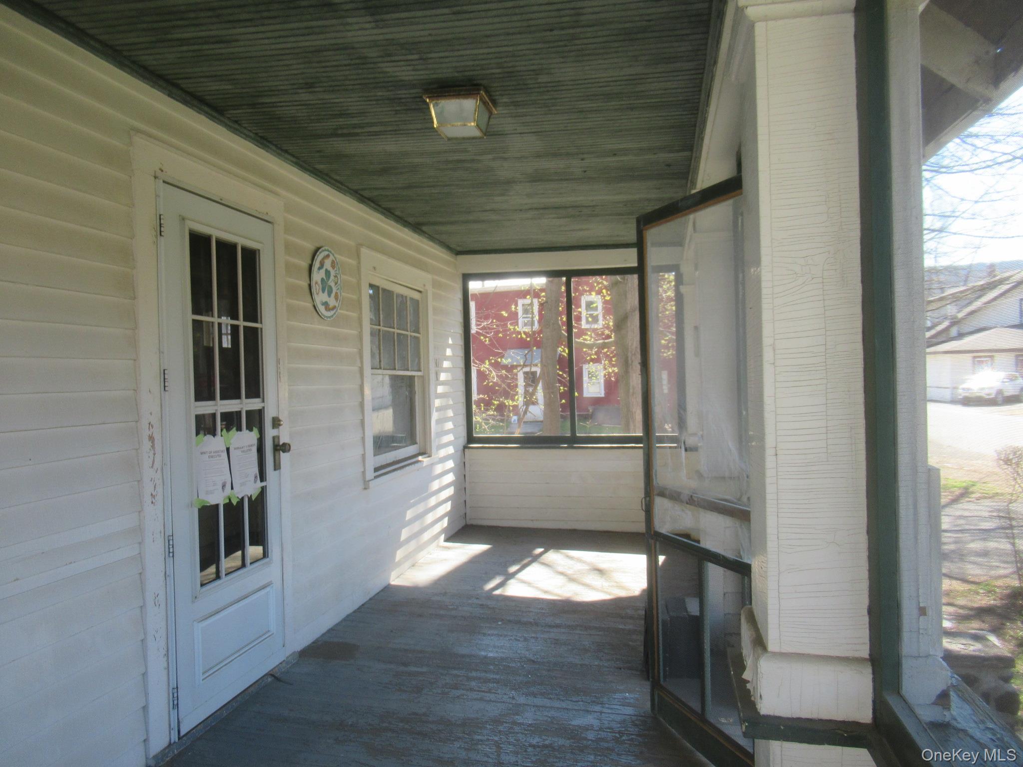 72 Waterstone Road Greenwood Lake, NY 10925 - Photo 16 of 20 Covered porch featuring white siding, a glass-paneled entry door, a sash window, a dark green painted ceiling, and enclosed screening