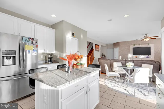 a living room with stainless steel appliances kitchen island granite countertop a table chairs and a refrigerator
