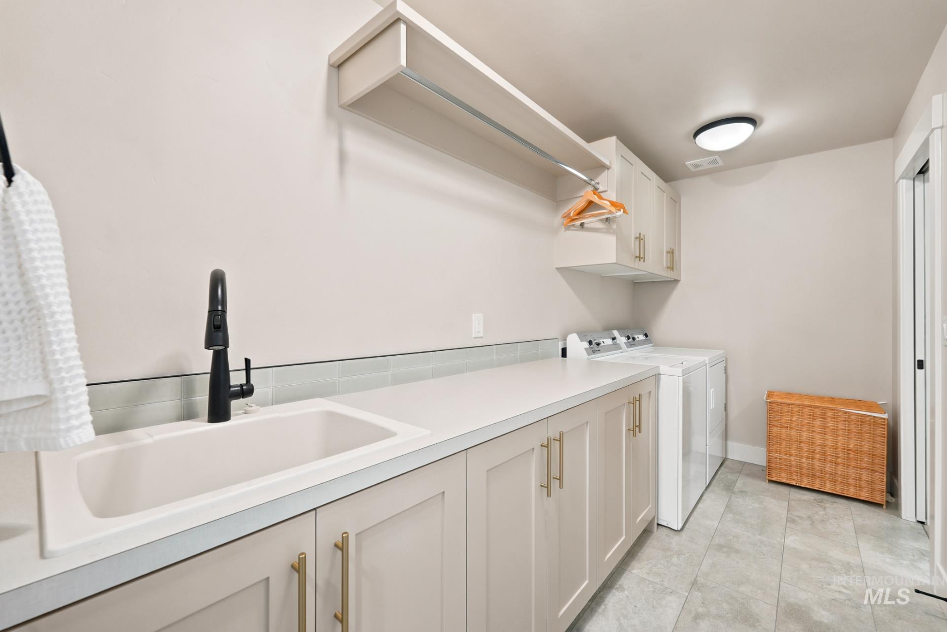 6933 South Zenith Avenue Meridian, ID 83642 - Photo 21 of 34 Laundry room featuring a white integrated sink with a matte black faucet, light grey cabinetry with gold-toned hardware, and a light grey tile backsplash