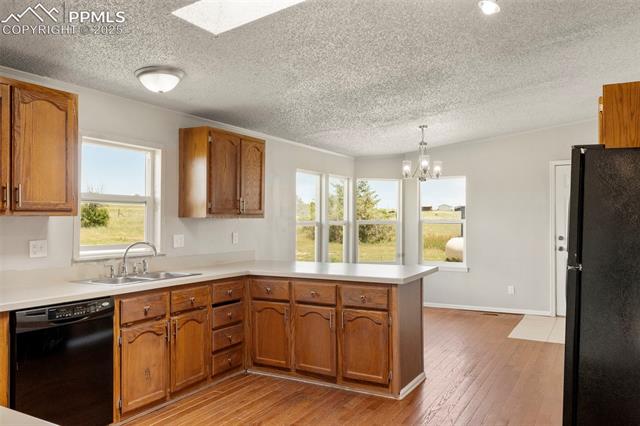 34535 Big Springs Road Yoder, CO 80864 - Photo 9 of 34 Kitchen with black appliances, a peninsula, a textured ceiling, brown cabinets, and light countertops