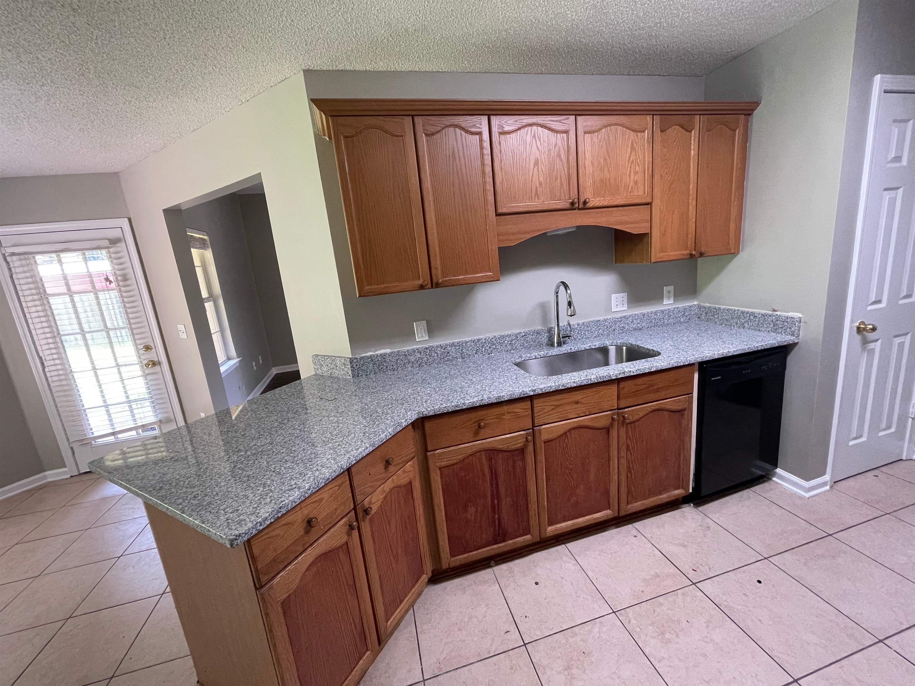 4580 Sun Ridge Drive Memphis, TN 38128 - Photo 5 of 16 Kitchen featuring black dishwasher, a textured ceiling, light tile patterned flooring, brown cabinetry, and light stone counters