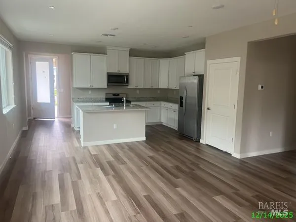 a living room with stainless steel appliances a refrigerator a stove top oven a wooden floor and a window