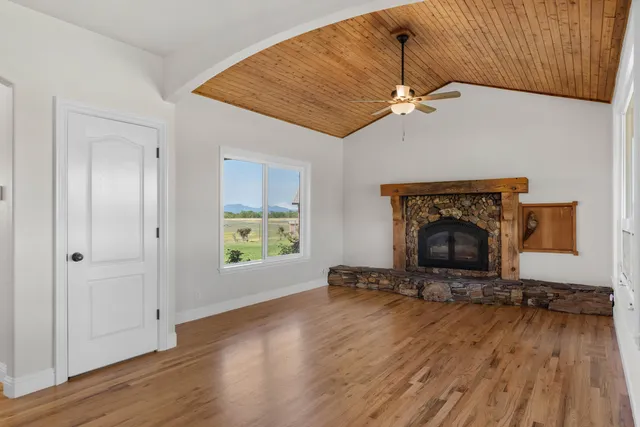an empty room with wooden floor a fireplace a ceiling fan and a window