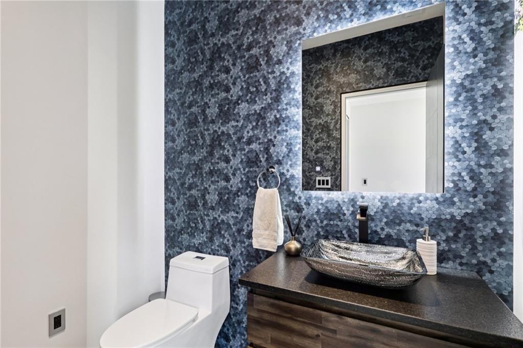 646 Science Street Pittsburgh, PA 15210 - Photo 17 of 35 Completing the main level is a thoughtfully designed powder room that blends style with sophistication. Engineered hardwood flooring adds warmth underfoot, while two incredible tiled feature walls bring texture and visual interest. A backlit mirror provides both function and ambiance, making this space as inviting as it is refined.