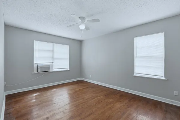 an empty room with wooden floor chandelier fan and windows