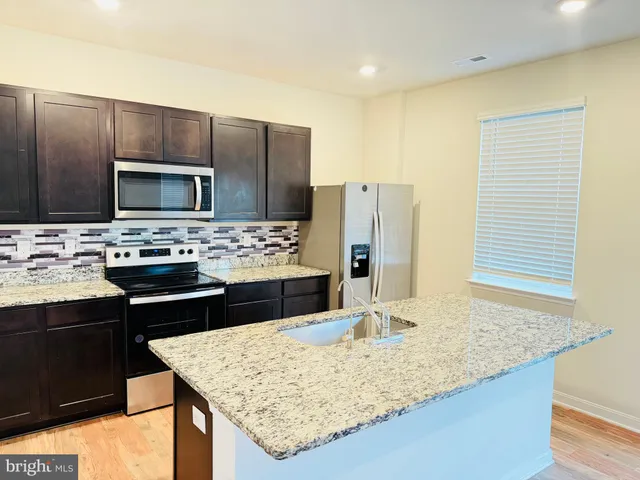 a kitchen with kitchen island granite countertop wooden cabinets refrigerator and stove