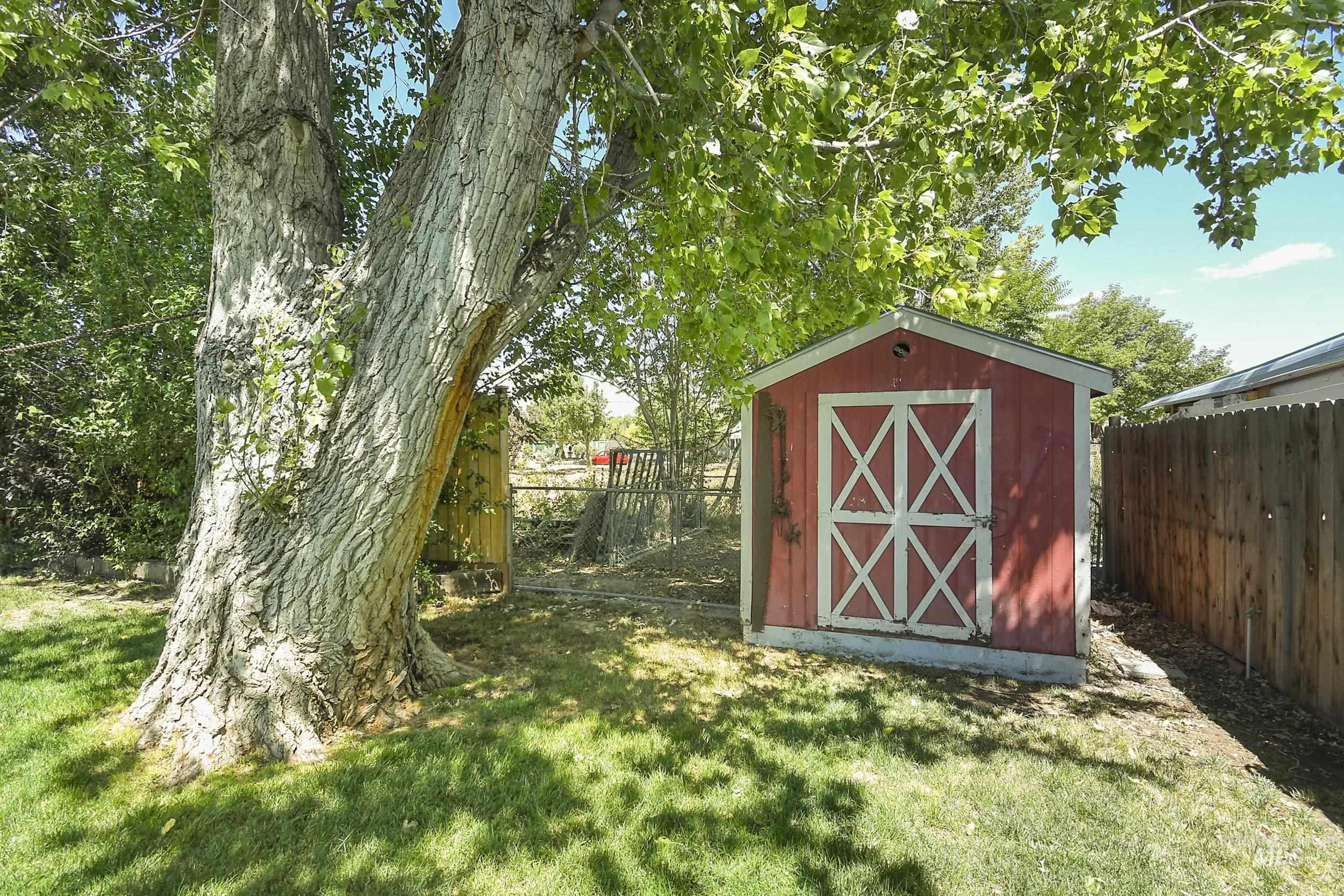1108 East Ustick Road Caldwell, ID 83607 - Photo 29 of 30 Backyard featuring a red storage shed with white cross-braced doors, a mature tree providing shade, a wood privacy fence, and a chain-link fence