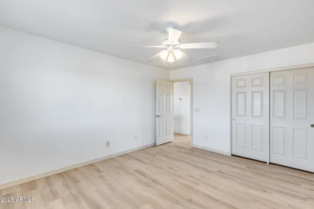 an empty room with wooden floor fan and windows