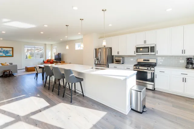 a open kitchen with stainless steel appliances kitchen island granite countertop a stove top oven a sink a dining table and chairs with wooden floor