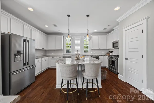 a kitchen with stainless steel appliances granite countertop a dining table chairs refrigerator and wooden floor