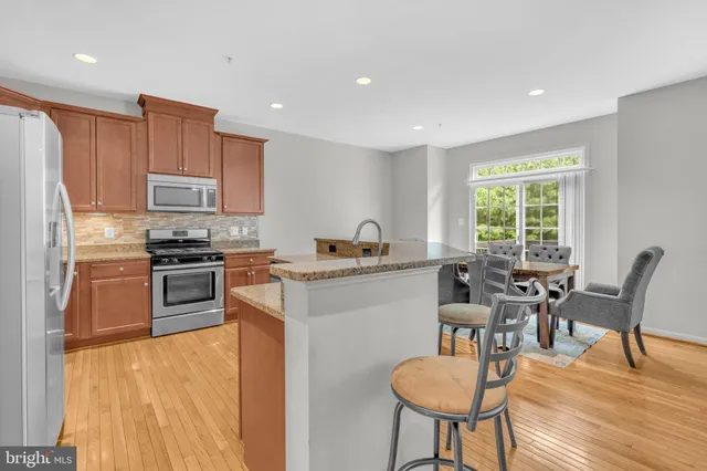 a kitchen with stainless steel appliances granite countertop a stove top oven a sink a refrigerator with a dining table and chairs with wooden floor