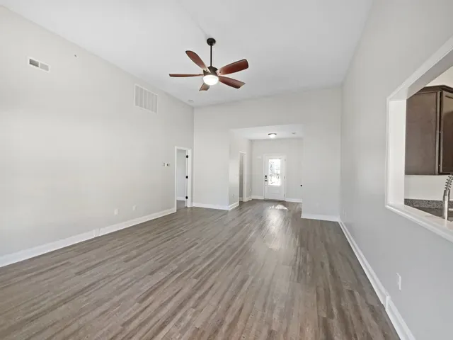 an empty room with wooden floor a ceiling fan and windows
