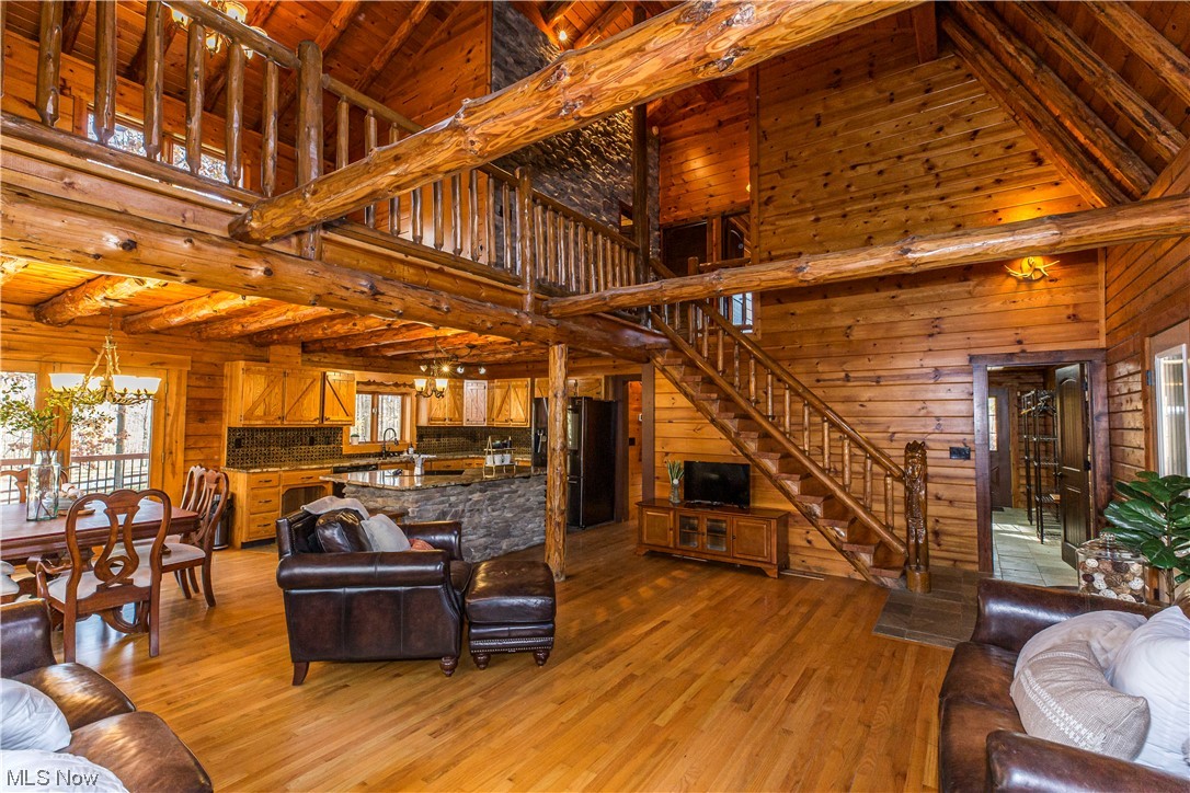 Living room with light hardwood / wood-style floors, beamed ceiling, wooden walls, high vaulted ceiling, and an inviting chandelier
