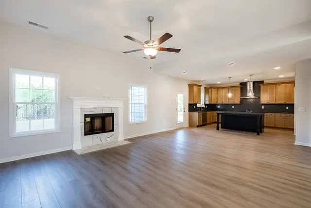 a view of an empty room with wooden floor and a kitchen