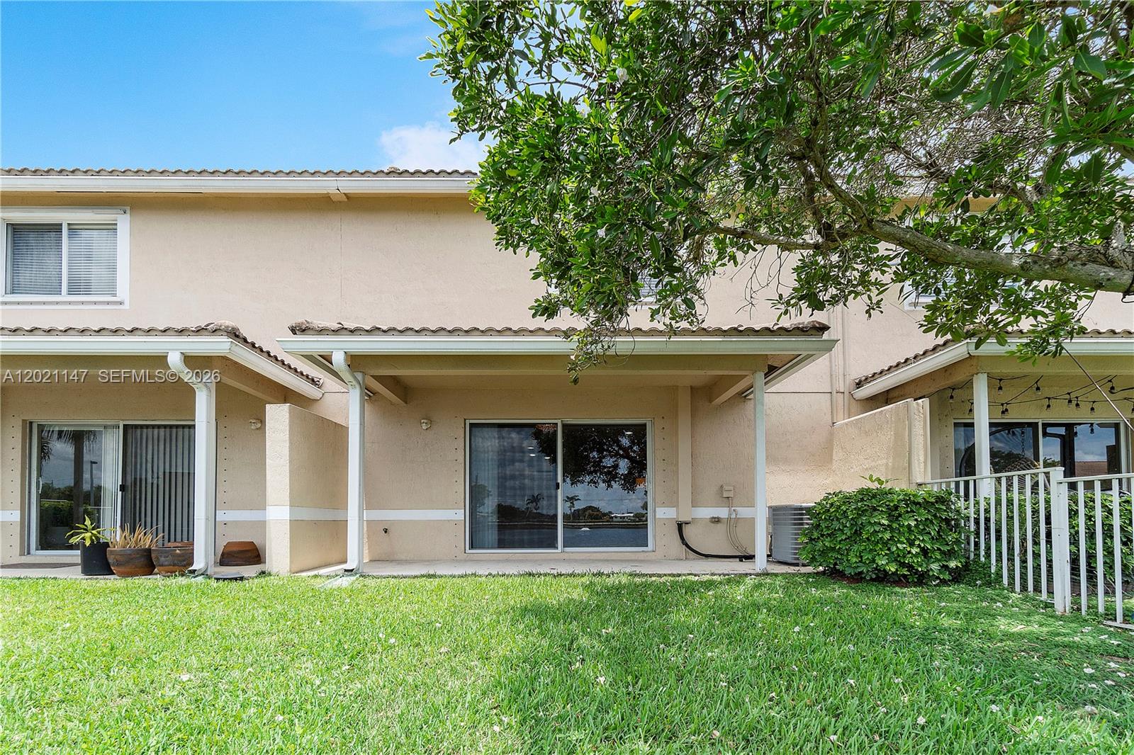 5930 Abbey Road Tamarac, FL 33321 - Photo 15 of 26 a view of a white house with a big yard and potted plants and a large tree