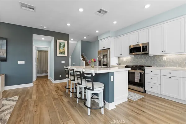 a kitchen with stainless steel appliances granite countertop a stove top oven a sink dishwasher a dining table and chairs with wooden floor