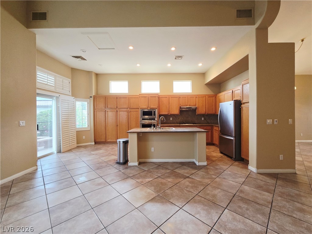 1265 Moon Vision Street Henderson, NV 89052 - Photo 13 of 35 Kitchen with stainless steel appliances, a kitchen island with sink, light tile patterned floors, tasteful backsplash, and light countertops