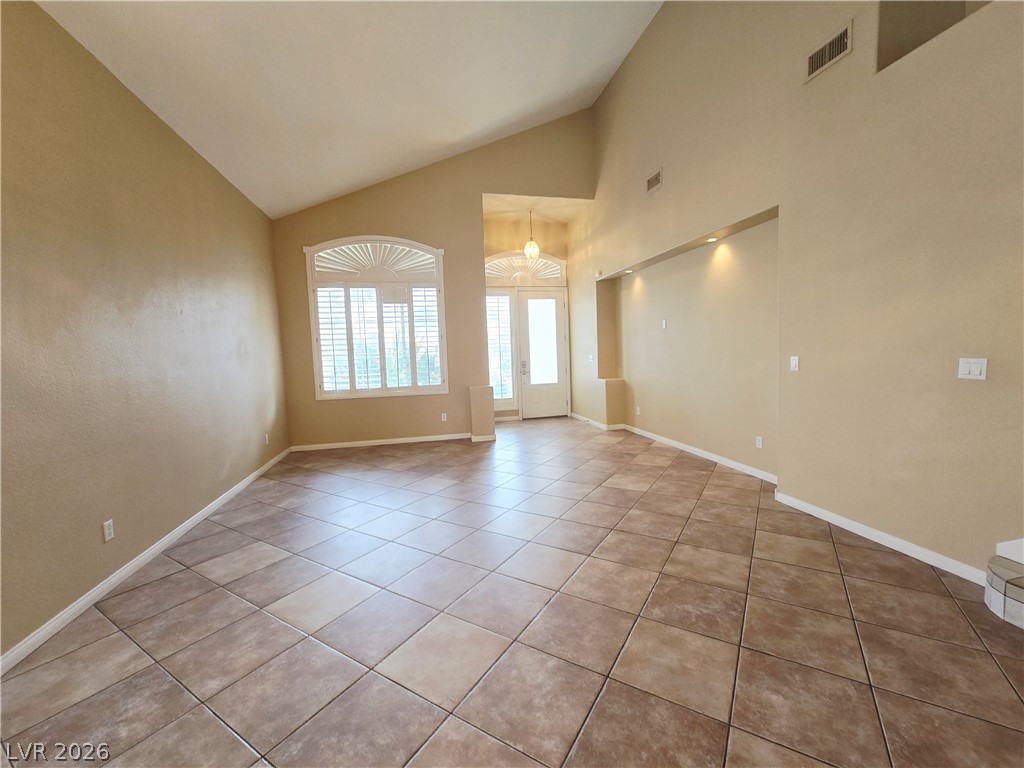 1265 Moon Vision Street Henderson, NV 89052 - Photo 5 of 35 Empty room with light tile patterned flooring, lofted ceiling, and suspended lighting